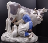 Auktion 339 / Los 8041 <br>Frau melkt eine Kuh, während die Katze zuschaut " Bing &amp; Gröndahl " Nr. 2017, H. 18,5cm, l. 19cm, ein Horn beschädigt