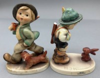 Auktion 364 / Los 9030 <br>2x Hummel-Figuren, Jäger und Wanderbursche mit Hund bzw. Hasen, beide beschädigt, H-ca. 12 und 13 cm