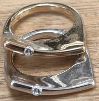 Auktion 361 / Los 1229 <br>2x leicht gebogene Ringe "Pierre Lang"je ein klarer Stein, silber-und goldfarben, beide RG 55