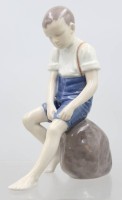 Auktion 370 / Los 8143 <br>Junge auf Stein sitzend, Bing und Gr&ouml;ndahl, am Sockel monogr. IPI, Entw. Ingeborg Plockross Irminger, Modelnr. 1757, Unterglasurbemalung, H- 19,5cm