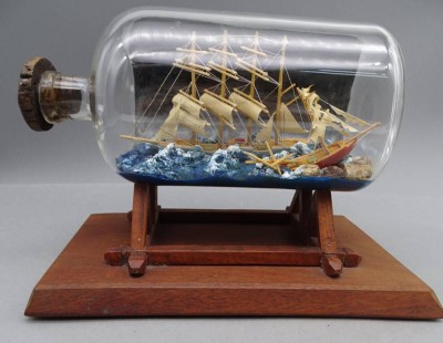 Auktion 352<br>Buddelschiff in schwerer See mit Felsen,  in gr. Flasche, H- mit Ständer 19 cm, L-25 cm [1]