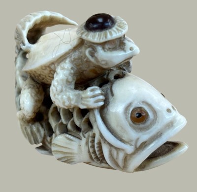 Auktion 367<br>Netsuke, Frosch auf Fisch, Taguanuss, Japan, signiert auf eingelegter Perlmutt-Platte, L-5 cm, H-3 cm [1]